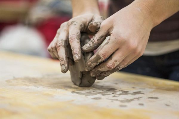 An artist’s clay-covered hands carefully shaping a sculpture
